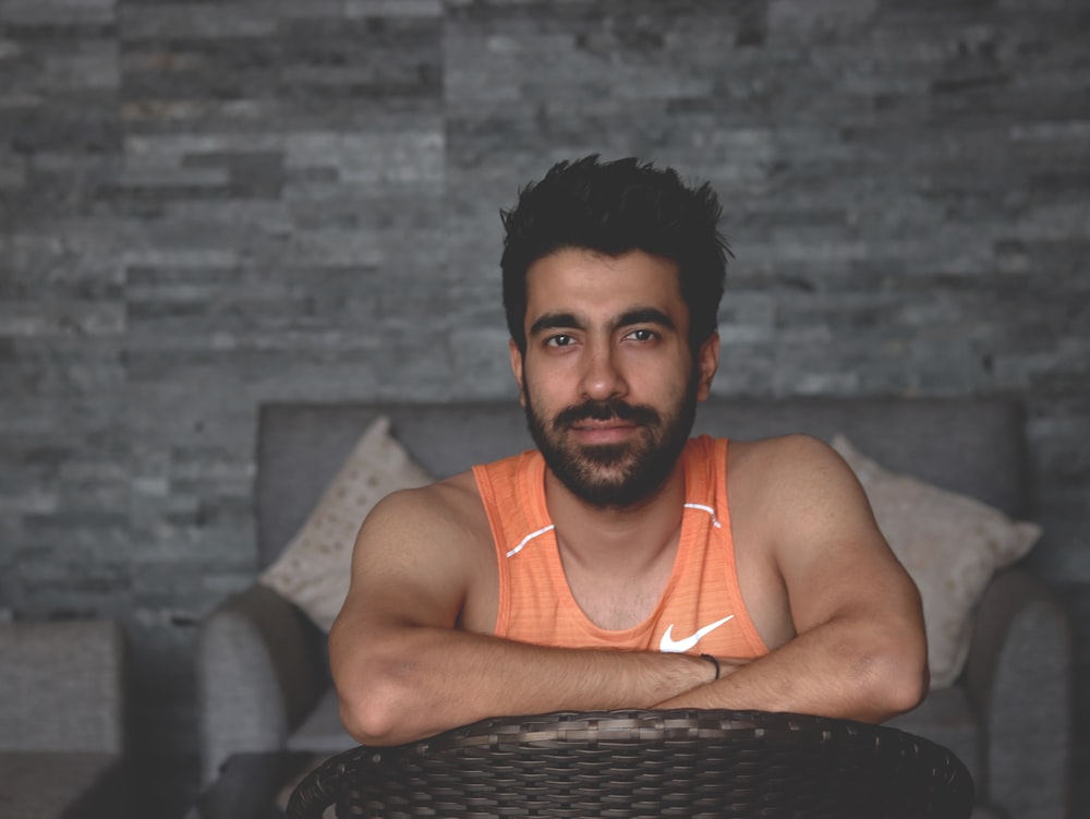 man in orange tank top sitting on couch