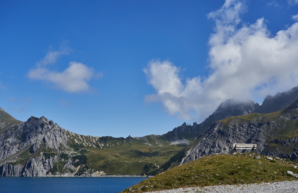 green and gray mountain beside body of water under blue sky during daytime