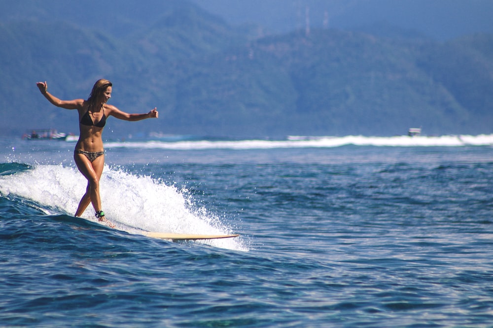 woman in black bikini surfing on sea during daytime