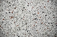 A close-up view of a terrazzo surface featuring a pattern of variously sized and shaped stones embedded in a smooth, light-colored matrix. The stones are predominantly black and brown, creating a speckled effect across the entire surface.