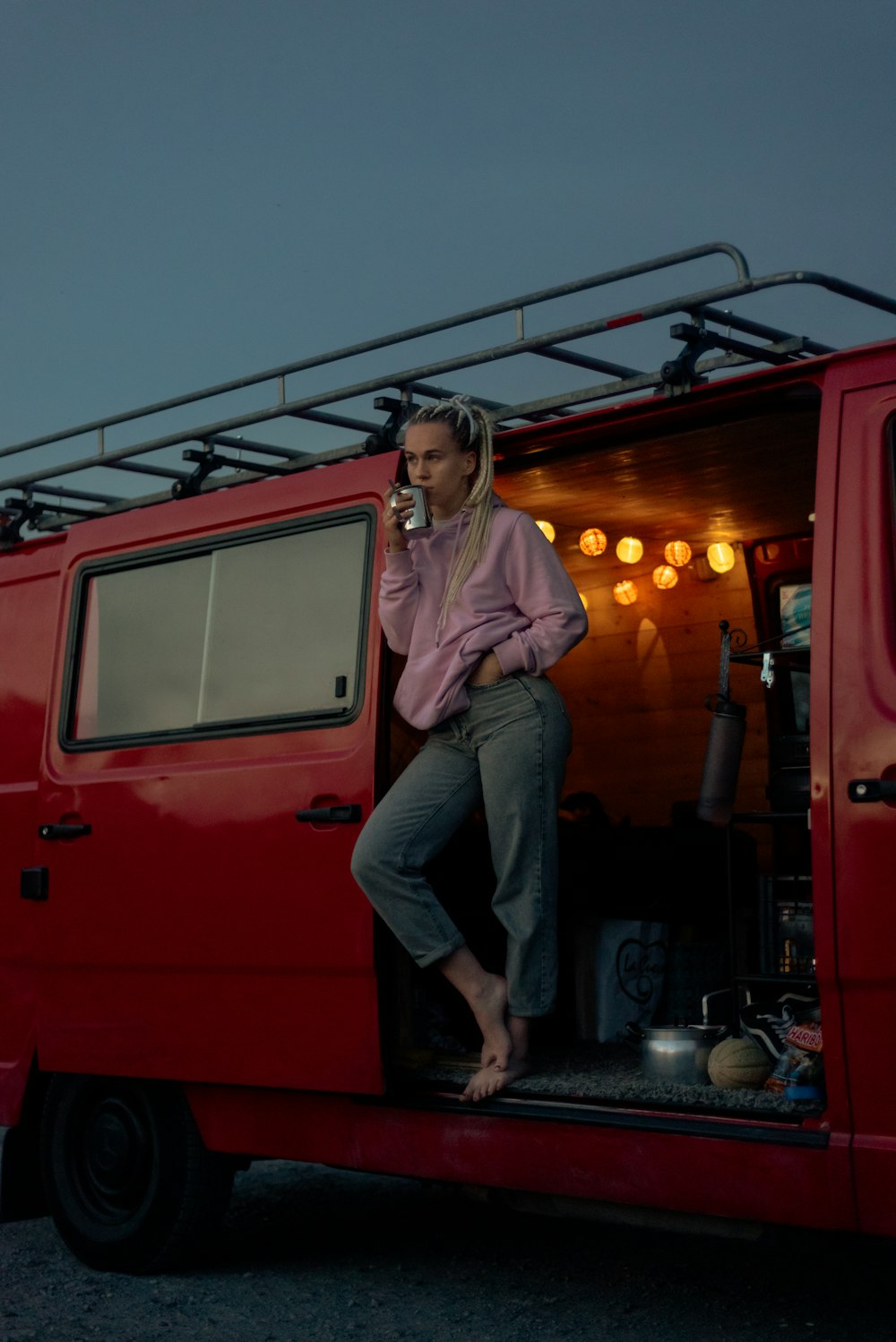 woman in white long sleeve shirt and black pants standing beside red car