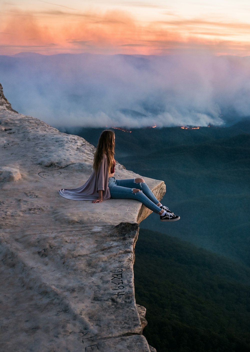 Frau in blauen Jeans sitzt tagsüber auf einer Felsformation