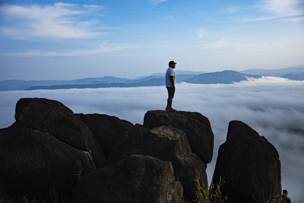 man in black t-shirt standing on rock formation near body of water during daytime