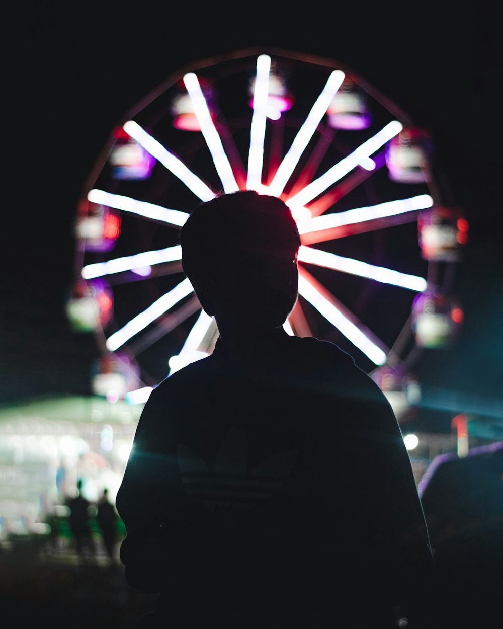 man in black shirt standing in front of lighted ferris wheel