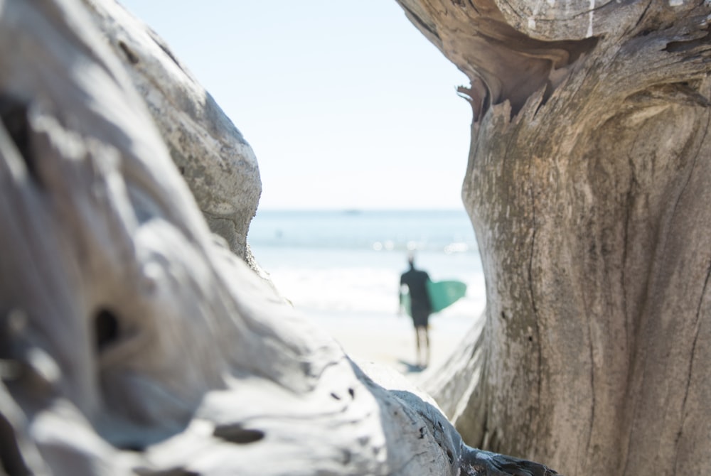 person in blue shirt and black pants standing on brown rock formation near body of water