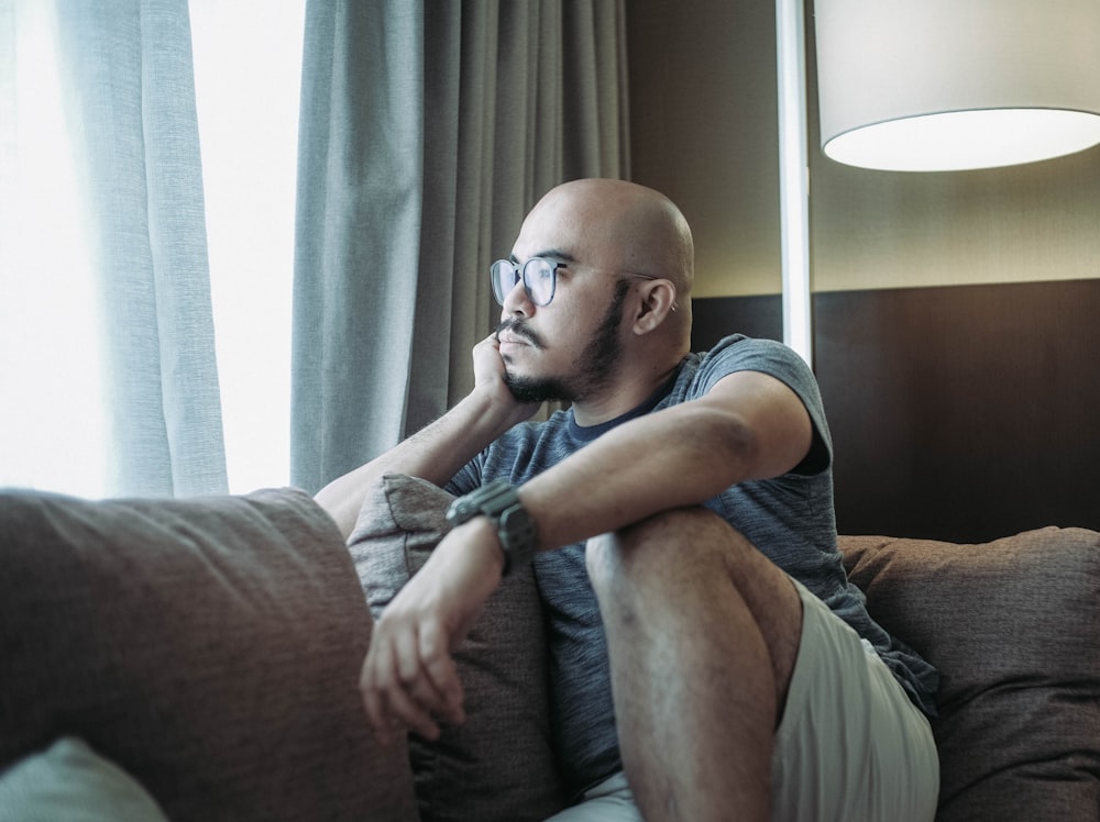 man in black crew neck t-shirt wearing black framed eyeglasses sitting on brown sofa