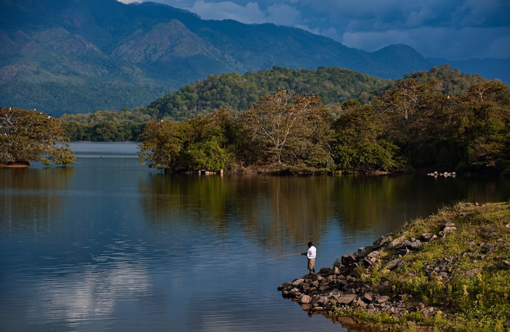 person in white shirt sitting on rock near body of water during daytime