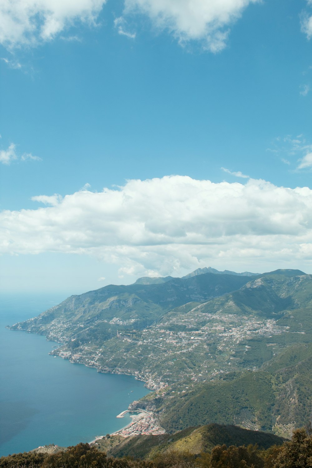 green and brown mountains beside blue sea under blue and white cloudy sky during daytime