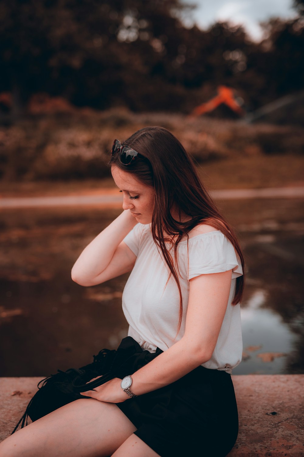 woman in white tank top and black pants wearing black sunglasses sitting on brown rock during