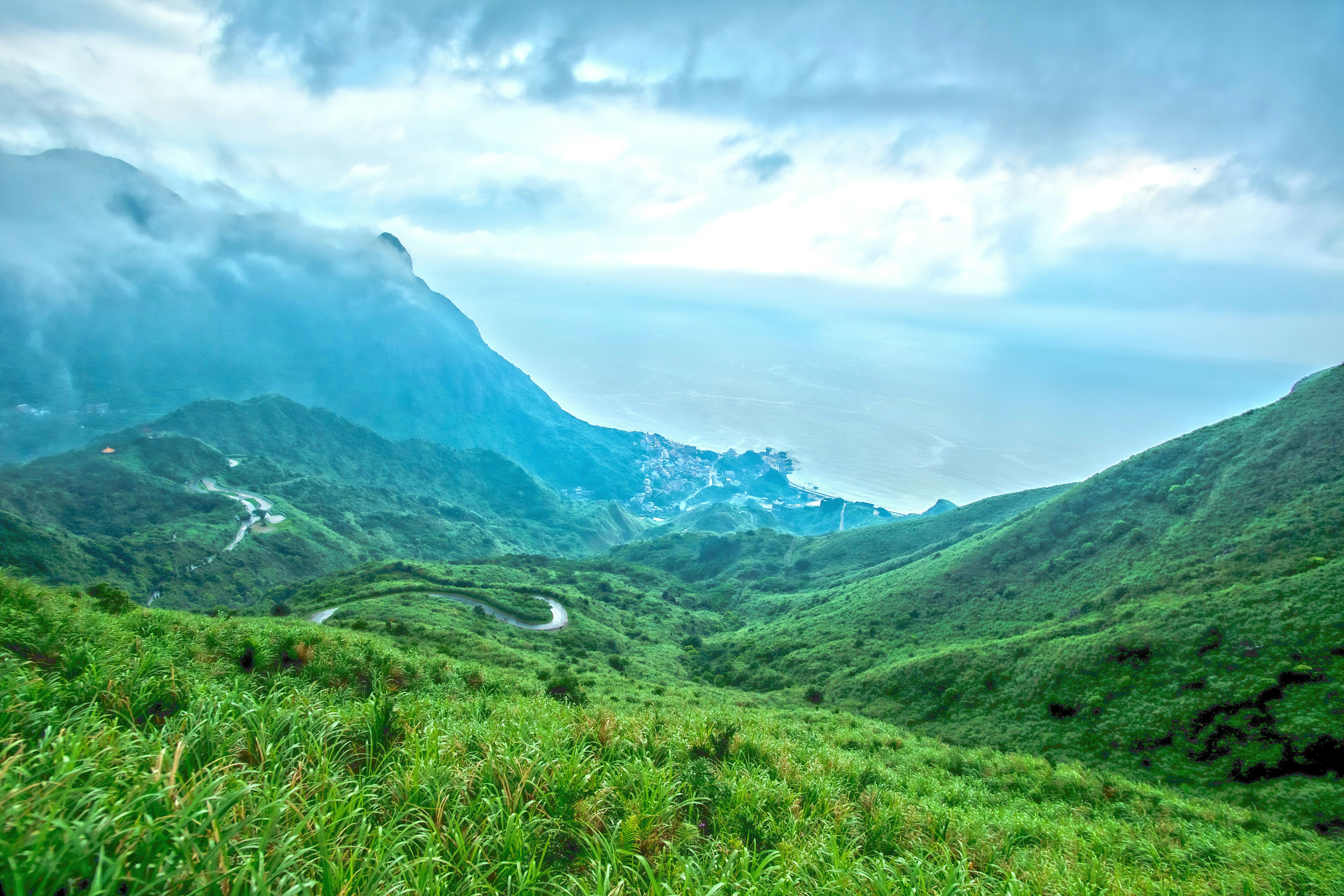 green grass field and mountains under white clouds and blue sky during daytime