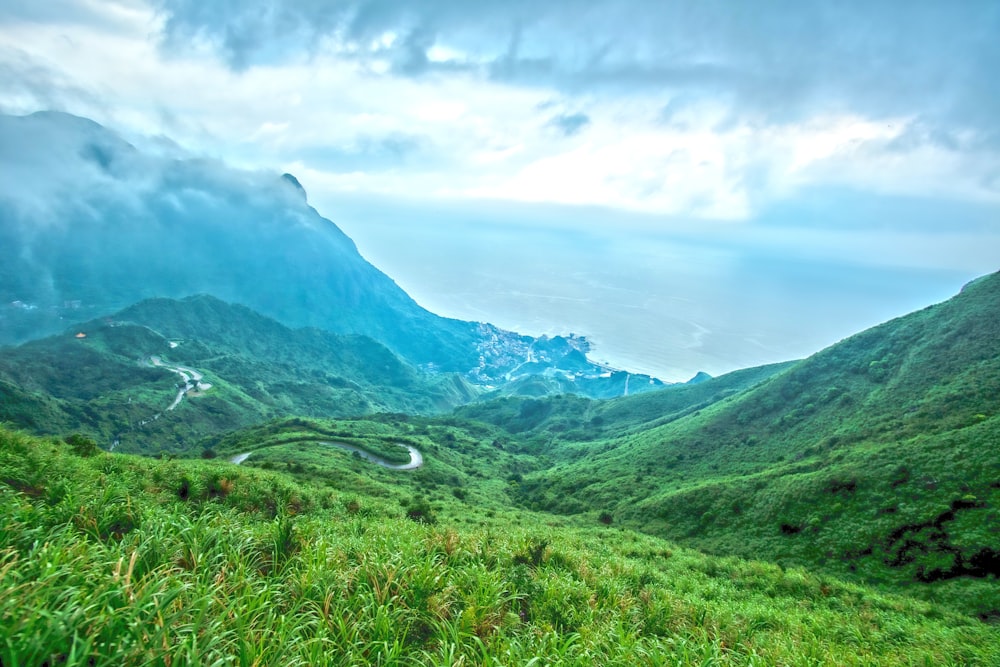 green grass field and mountains under white clouds and blue sky during daytime