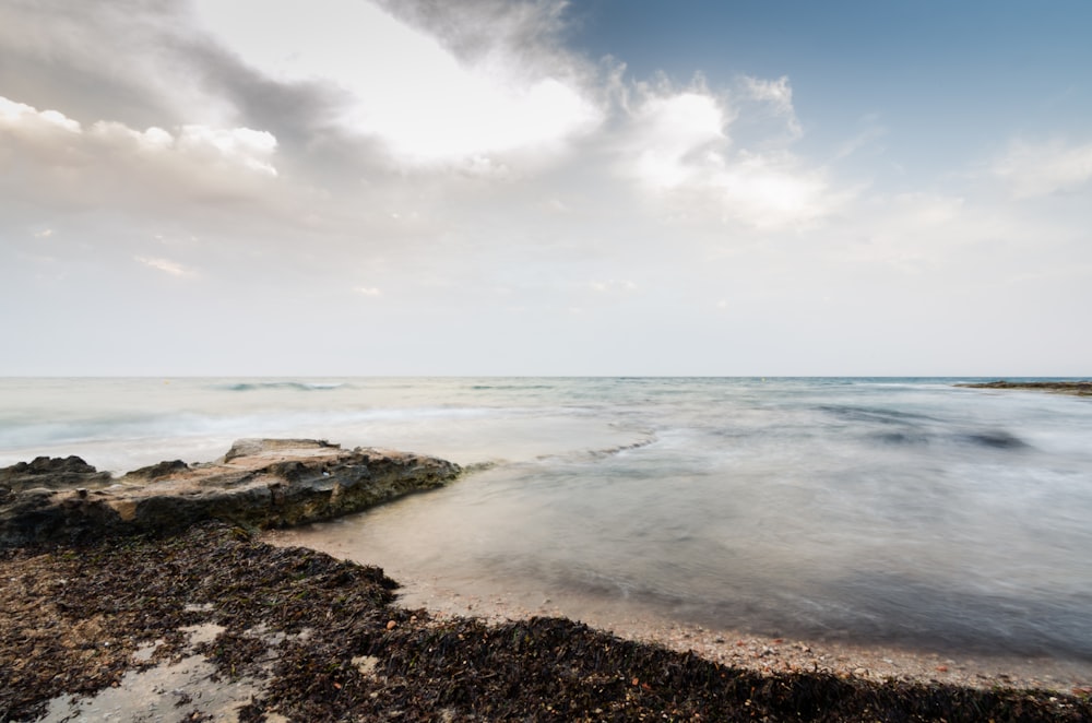 brown rock formation on sea under white clouds and blue sky during daytime