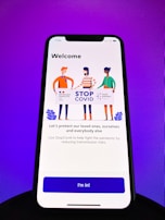 A smartphone screen displays a welcome screen for the StopCovid app. Three illustrated figures hold a sign with logos and text promoting the StopCovid initiative. The message encourages protecting loved ones and reducing transmission risks.