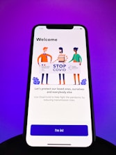 A smartphone screen displays a welcome screen for the StopCovid app. Three illustrated figures hold a sign with logos and text promoting the StopCovid initiative. The message encourages protecting loved ones and reducing transmission risks.