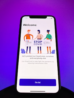 A smartphone screen displays a welcome screen for the StopCovid app. Three illustrated figures hold a sign with logos and text promoting the StopCovid initiative. The message encourages protecting loved ones and reducing transmission risks.
