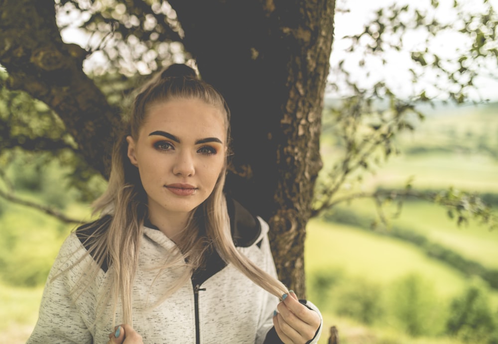 girl in white zip up jacket standing beside brown tree during daytime