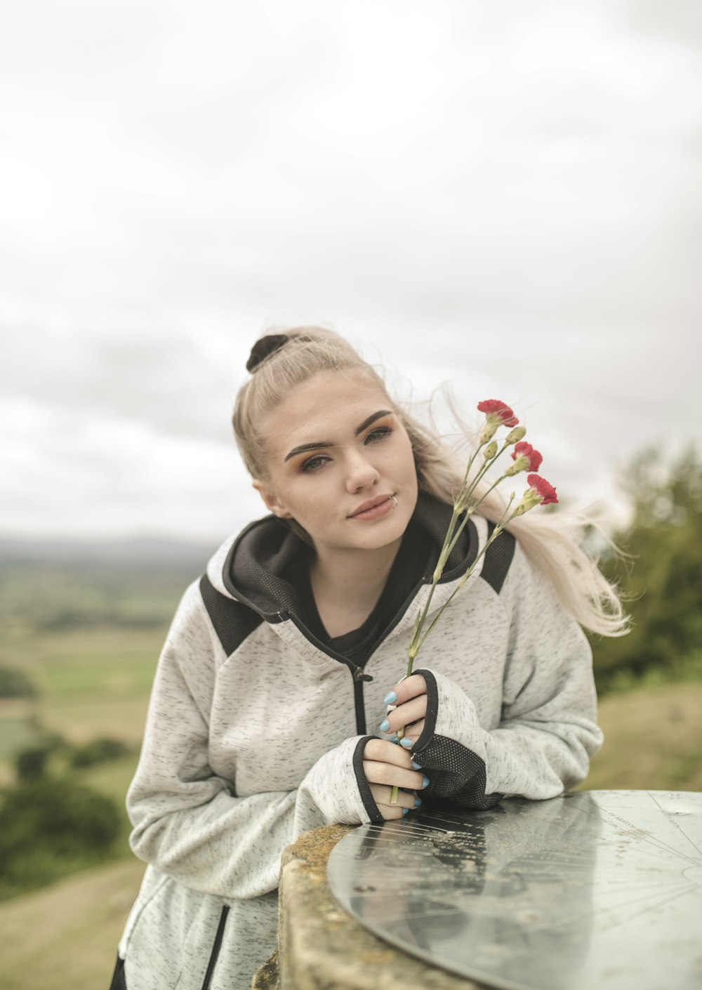 woman in gray and black hoodie holding red flower