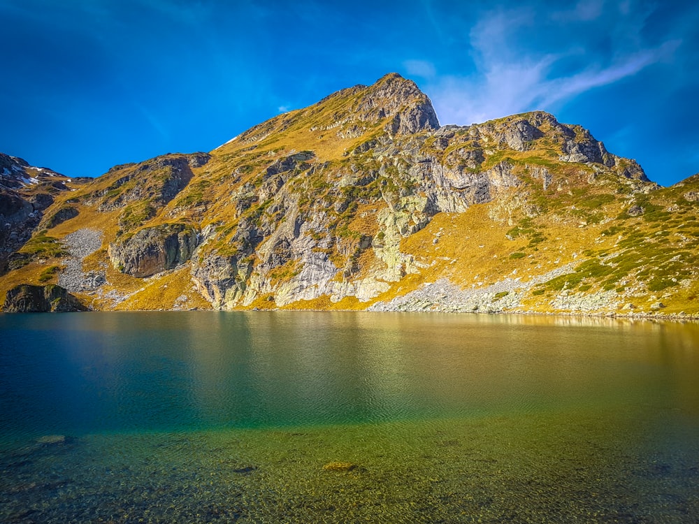 grüner See neben braunem und grünem Berg tagsüber unter blauem Himmel