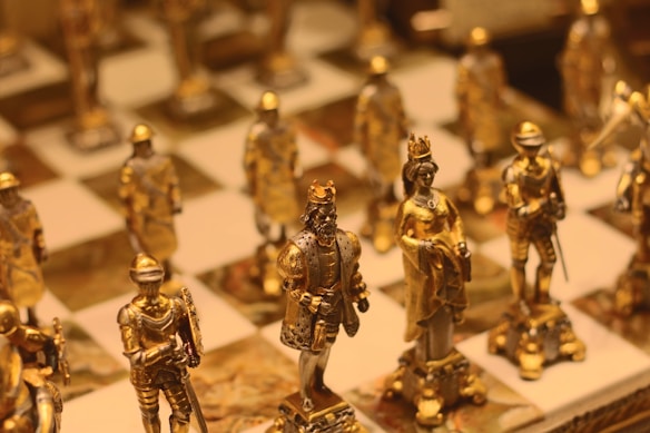 A close-up of intricately designed chess pieces with a focus on golden figures representing royalty and knights. The chessboard is elegant, with detailed craftsmanship on the pieces, highlighting a sense of luxury and historical significance.