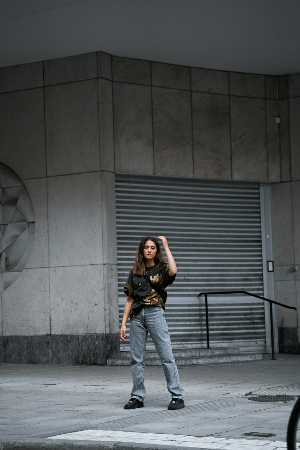 woman in black and brown long sleeve shirt and blue denim jeans standing beside gray wall
