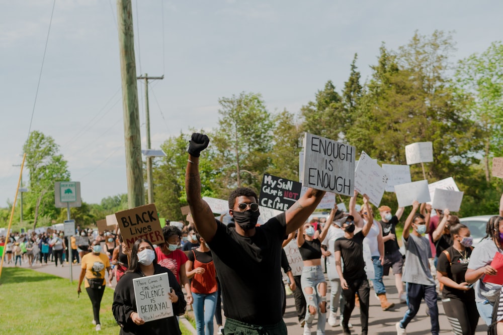 man in black crew neck t-shirt holding blue and white signage during daytime