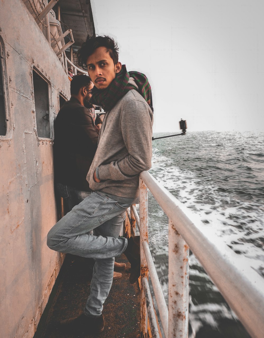 man in brown hoodie and blue denim jeans sitting on brown wooden railings