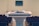 A wooden podium is positioned in a room with rows of empty seating, and a microphone rests on top. In the background, there is a blurred monitor on the wall, enhancing the setting's focus on public speaking or presentations.