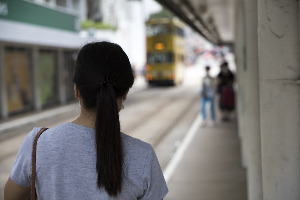 woman in gray shirt standing on sidewalk during daytime