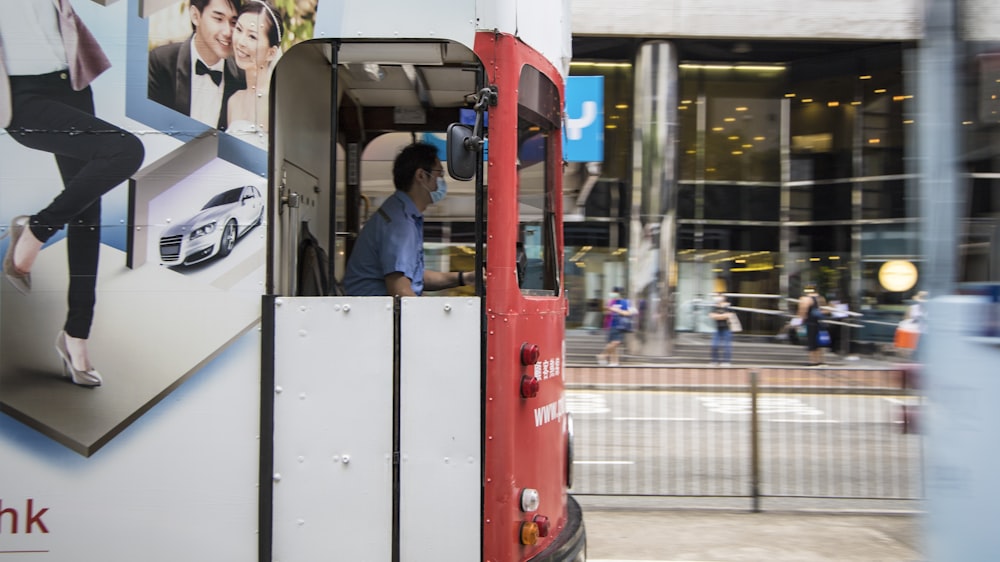 man in gray jacket sitting on red and white bus during daytime