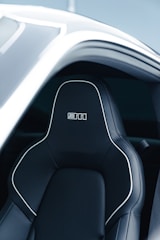 A sleek and modern car seat with black leather upholstery, featuring white stitching and a bold logo on the headrest. The seat is positioned within a partially open car door, revealing a stylish and futuristic design.