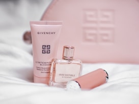 A collection of Givenchy cosmetics, including a tube of L'Intemporel Blossom cream, an Irresistible perfume bottle, and another cylindrical product, all set against a soft fabric background with a pastel pink Givenchy-branded pouch.