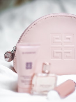 Soft pink leather pouch embossed with a geometric pattern, surrounded by luxury cosmetic items including a tube, a bottle of perfume, and a lipstick. The setup conveys a sense of elegance and sophistication.
