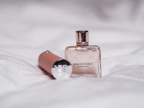 A bottle of Givenchy perfume labeled 'Irresistible' is placed on a white fabric surface. Beside the bottle lies a cylindrical object with a metallic cap.