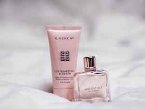 Two Givenchy beauty products are placed on a soft white surface. One is a pink tube labeled 'L'Intemporel Blossom' next to a square glass bottle of perfume labeled 'Irresistible'. The design is elegant and minimalist.