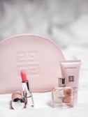 A collection of Givenchy beauty products is arranged neatly. A pink embossed makeup bag is in the background. In the foreground, a pink lipstick in a shiny silver tube is placed next to a clear glass perfume bottle labeled 'Irresistible Givenchy' and a pink tube of skincare product.