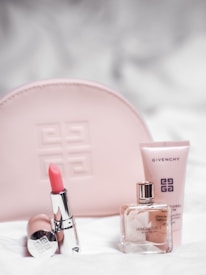 A collection of Givenchy beauty products is arranged neatly. A pink embossed makeup bag is in the background. In the foreground, a pink lipstick in a shiny silver tube is placed next to a clear glass perfume bottle labeled 'Irresistible Givenchy' and a pink tube of skincare product.