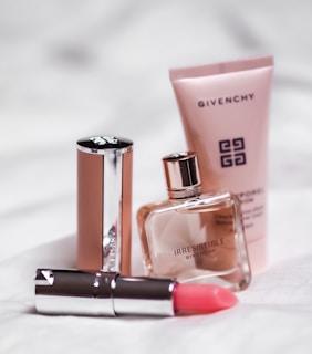 A collection of luxury beauty products, including a tube of pink lipstick, a small bottle of perfume, and a tube of lotion, all from the brand Givenchy. They are arranged on a soft, white surface that contrasts with the sleek, metallic and pastel packaging.