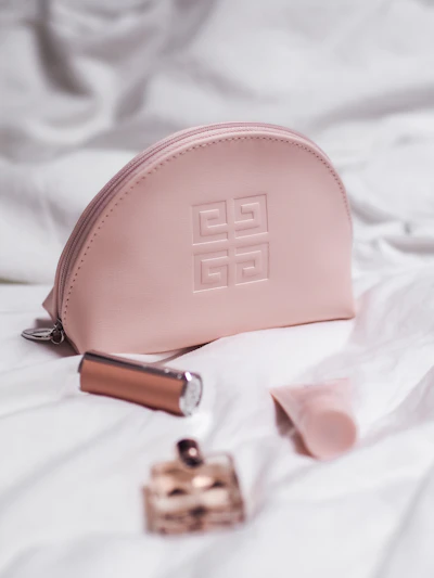 A sleek, soft pastel pink makeup bag with delicate gold zipper detailing displayed on a marble surface.