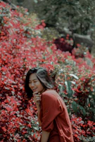 A joyful woman with natural hair laughing outdoors surrounded by blooming flowers.