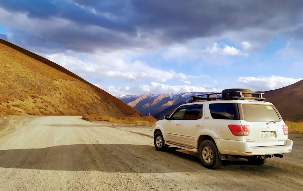 white suv on road near brown mountain under white clouds during daytime