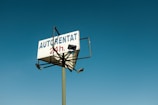 A tall sign with the words 'AUTORENTAT 24h.' is mounted on a pole against a clear blue sky. The sign is supported by a metal frame, and there are lights attached to it, indicating that it might be illuminated at night.