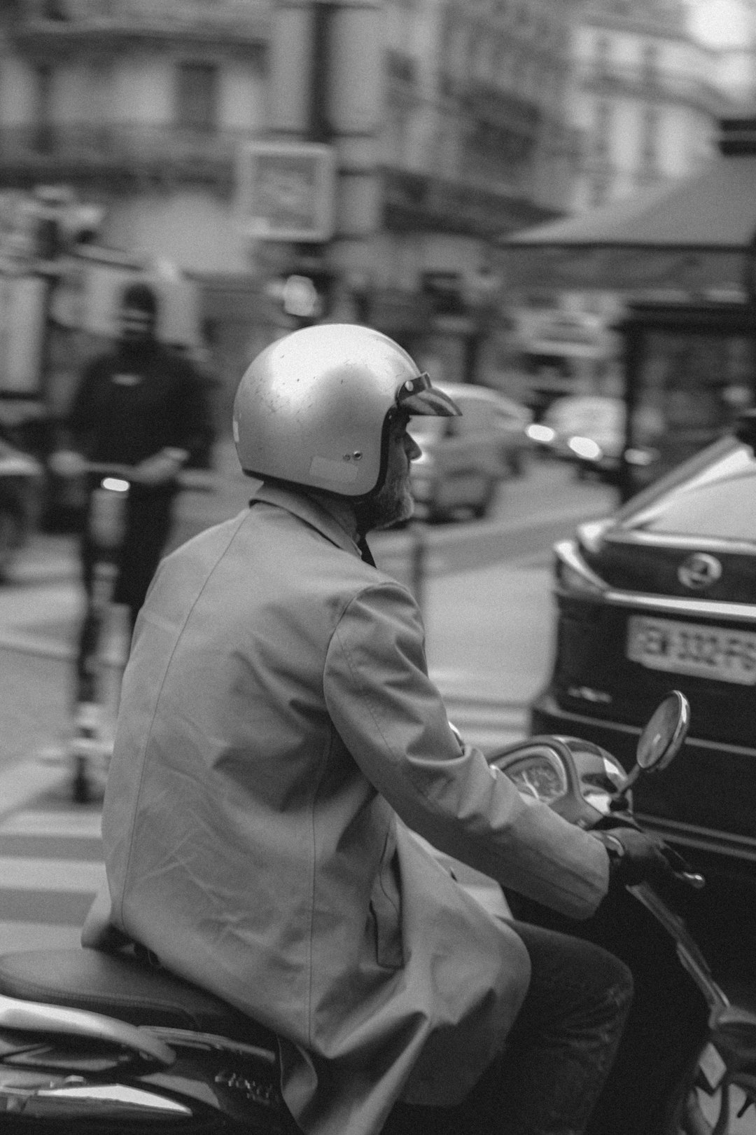 grayscale photo of man in gray coat and helmet riding motorcycle