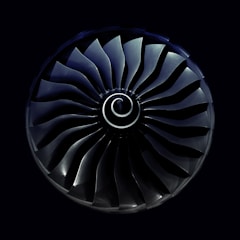 A symmetrical view of a jet engine turbine with curved blades radiating from a central spiral hub, set against a dark background.