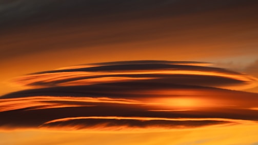 The image captures a stunning sunset or sunrise with the sky ablaze in hues of orange, yellow, and dark red. Cloud formations stretch across the sky, reflecting the vibrant colors and creating a dramatic and serene atmosphere.