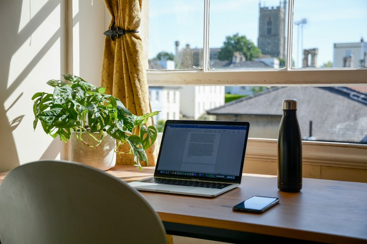 Person working on a laptop at a home desk with a coffee cup and notebook nearby
