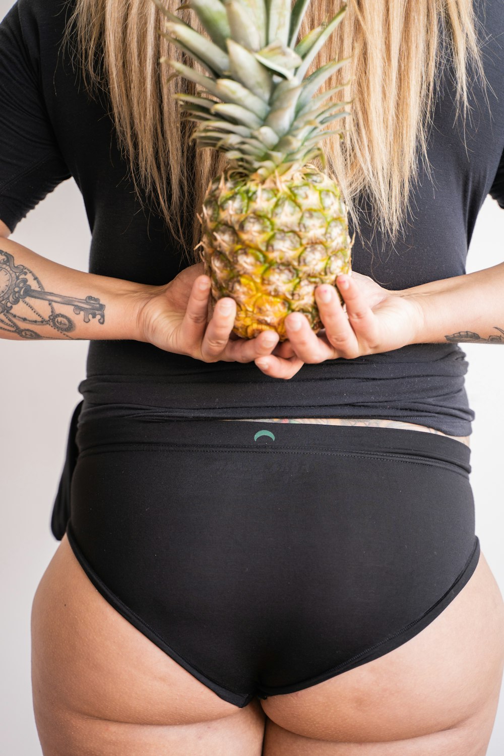 woman in black shirt and black skirt holding pineapple fruit