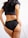 A woman is standing with her back turned, wearing black underwear and a cropped black top. Her long dark hair is visible, and she has one hand resting on her hip.