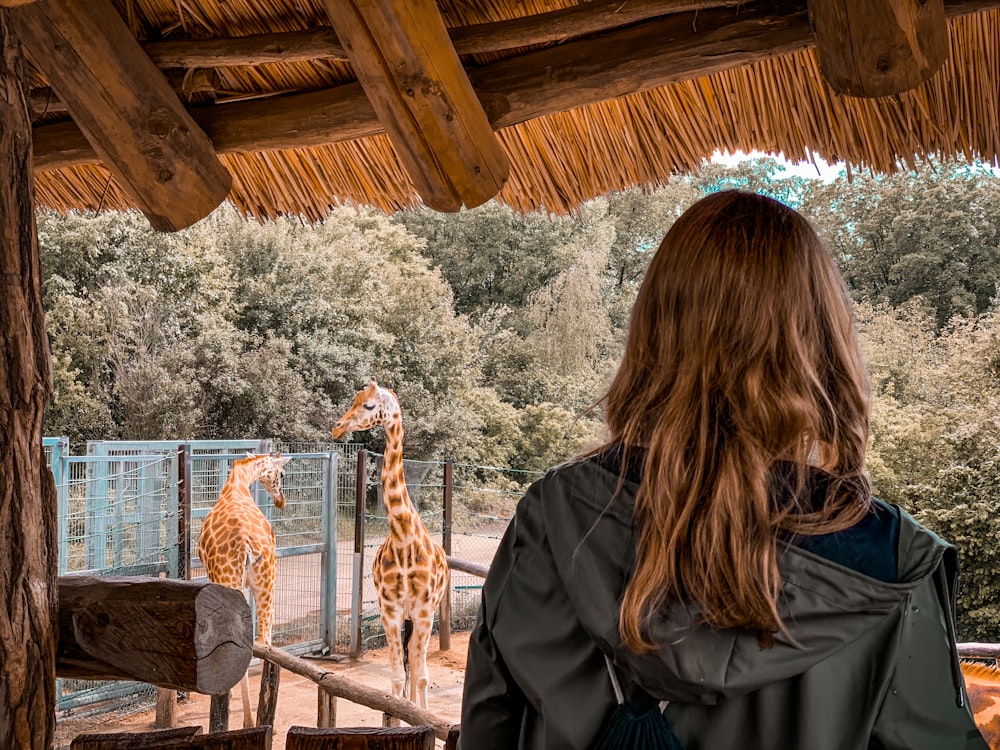 woman in black leather jacket standing beside giraffe during daytime