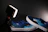 Close-up of a stylish pair of deep blue Makano Shoes glowing softly against a black background.