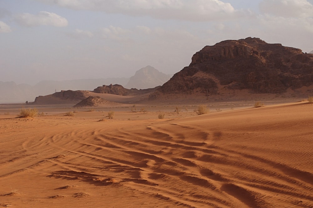 brown sand field near brown mountain under white sky during daytime